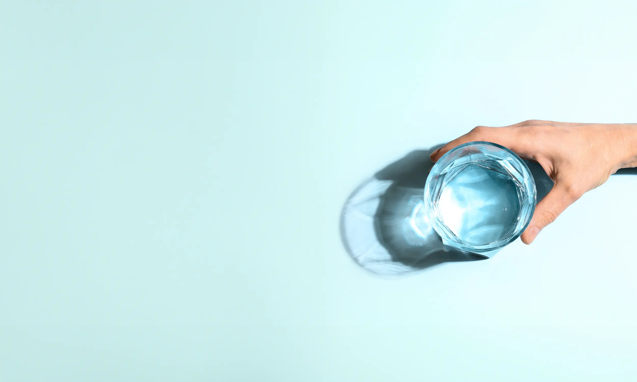 Glass of water in hand against a block blue background